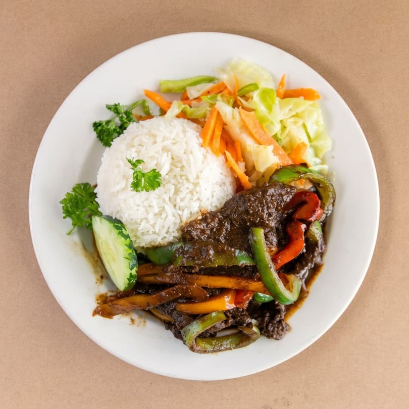 A plate of dark stewed meat with bell peppers, white rice, steamed cabbage, and carrots.