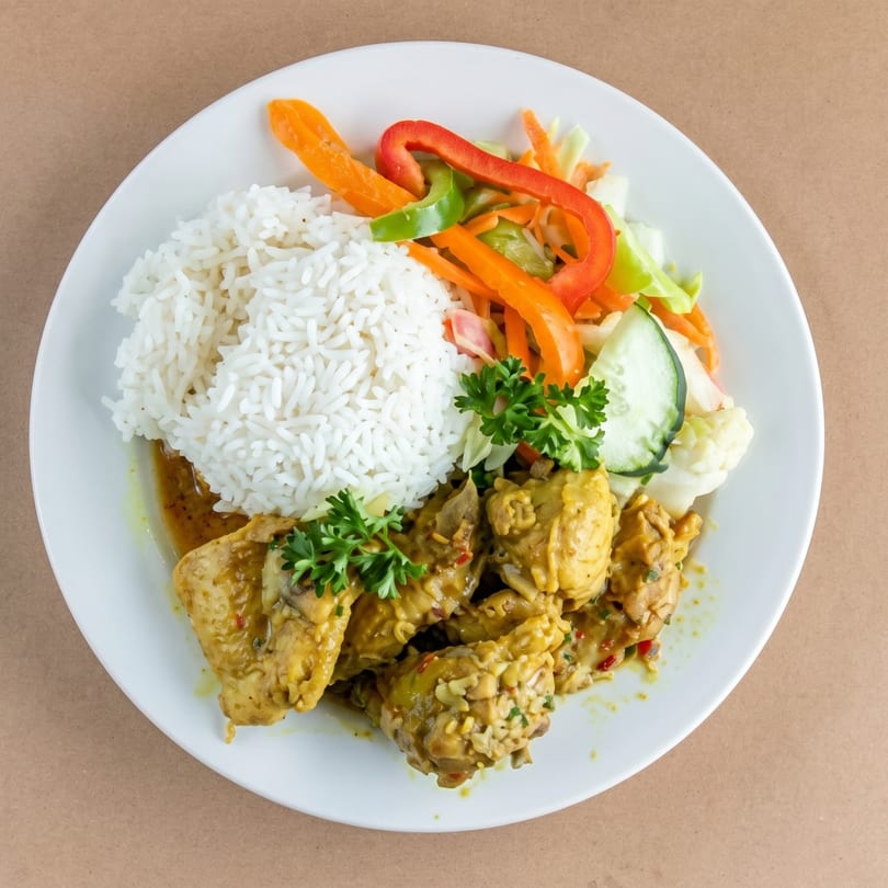 Curried chicken with white rice, fresh salad, and parsley on a white plate.