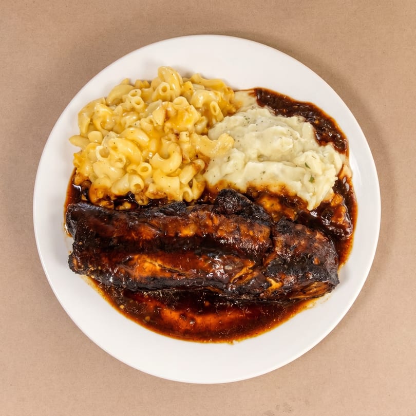 BBQ ribs with macaroni and cheese and mashed potatoes on a white plate.