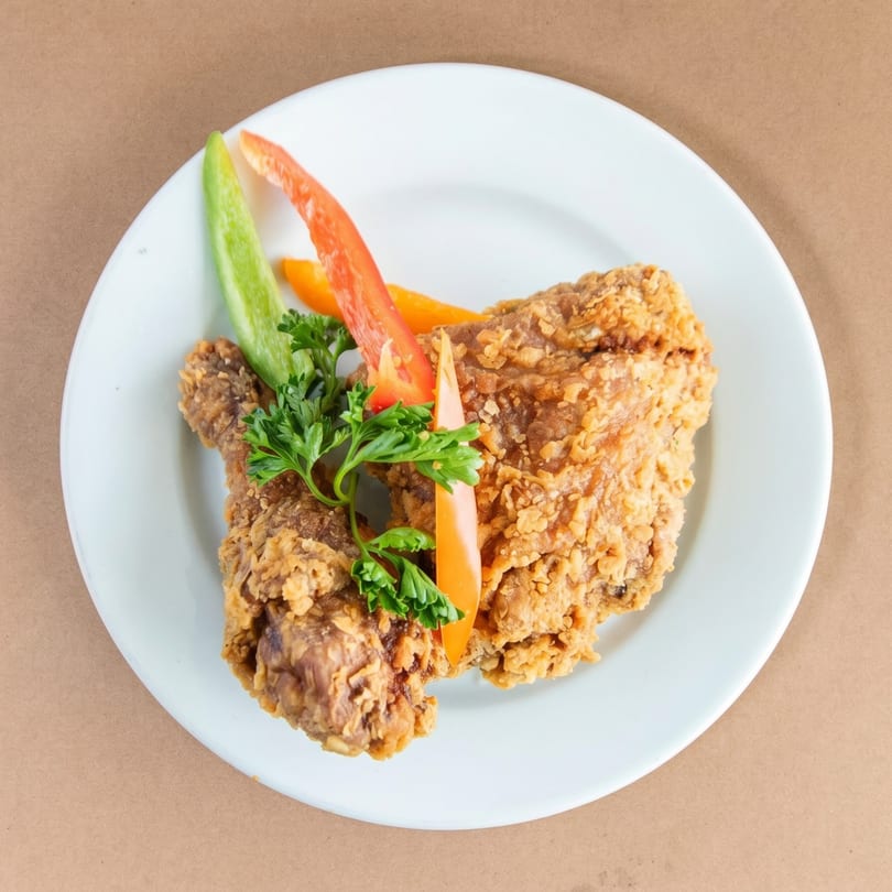 Crispy fried chicken pieces on a white plate, garnished with fresh parsley and colorful bell pepper strips.