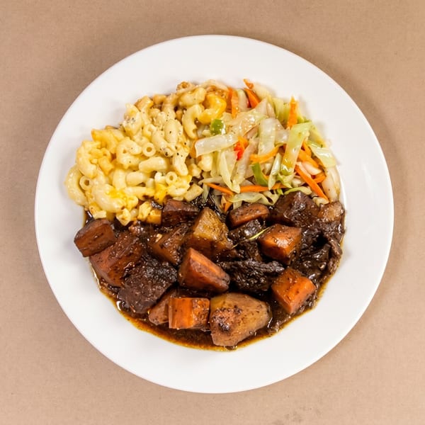 A white plate with stewed beef and carrots, macaroni and cheese, and sautéed cabbage.