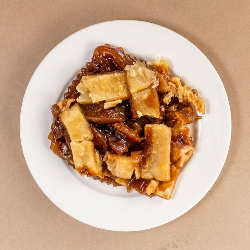A slice of apple pie with a lattice crust and gooey filling on a white plate.
