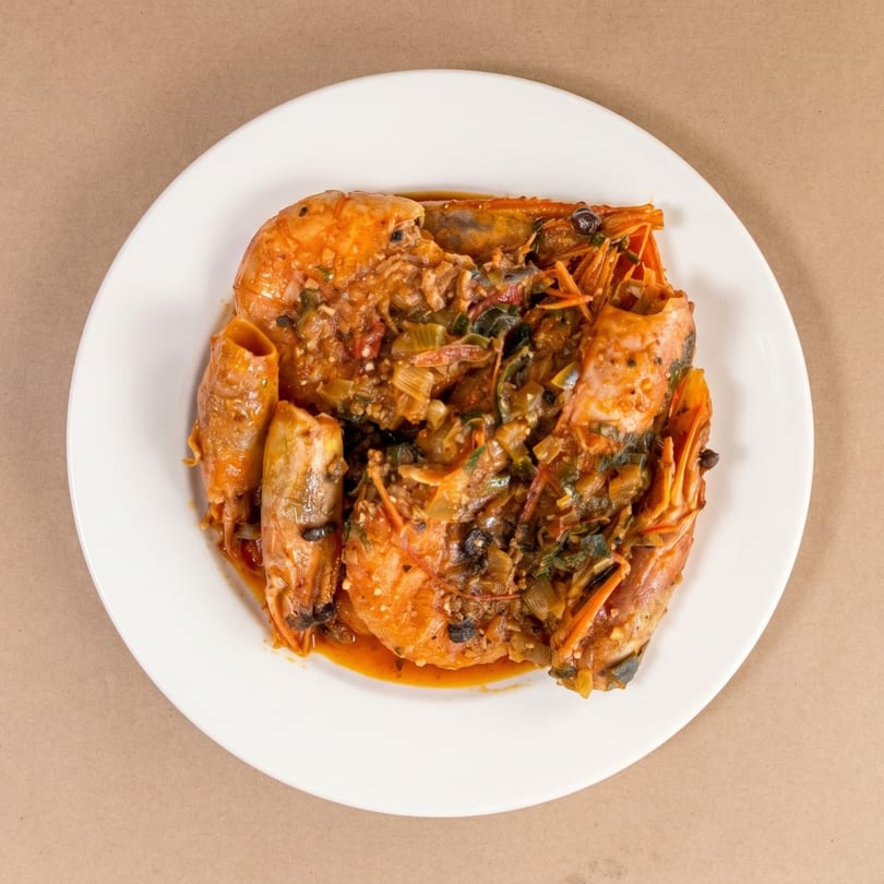 Top-down view of a white plate filled with large shrimp in a rich, dark red sauce.