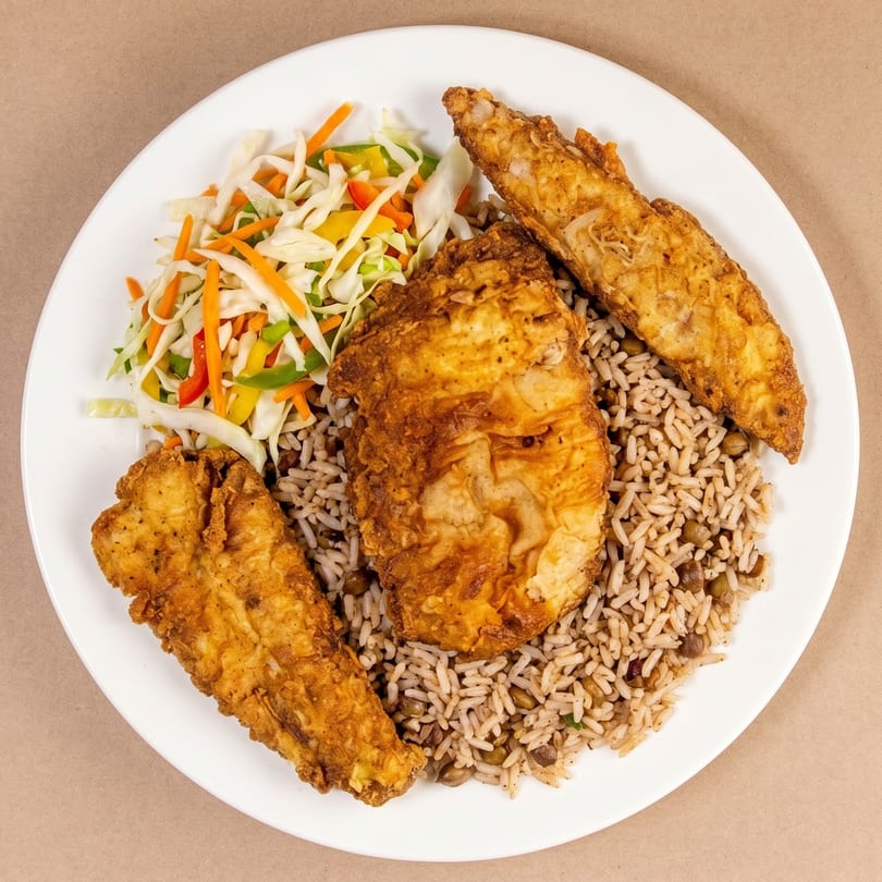 Fried fish fillets, rice and peas, and colorful coleslaw on a white plate.