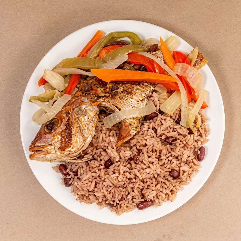 Fried fish with rice and beans, topped with sautéed peppers, carrots, and onions.