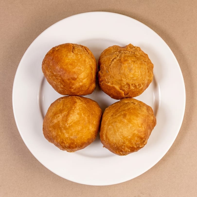 Four golden-brown fried dough balls, likely Jamaican festival dumplings, arranged on a white plate.